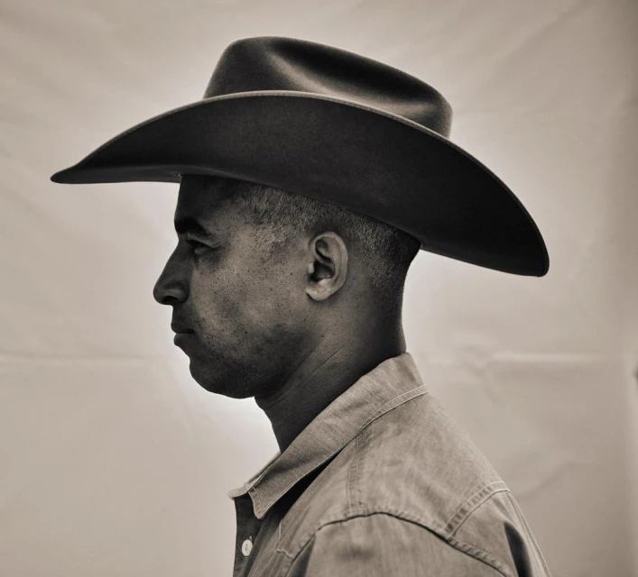 Monochromatic portrait of a man in a cowboy hat, side profile view, wearing a button-down shirt, set against a neutral background.
