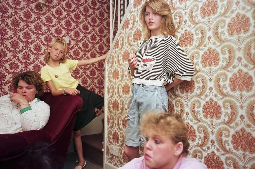 Four people in a room with patterned wallpaper, including an adult female, a teenager, a child, and a younger child.