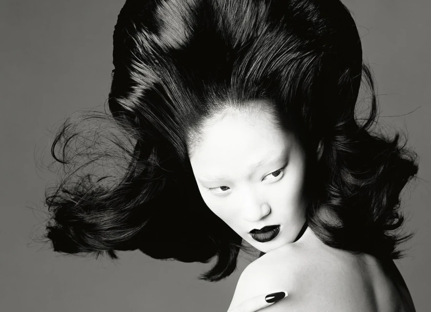 Monochrome portrait of Asian model with dramatic black hair and lipstick, neutral gray backdrop, beauty shot, high fashion editorial.