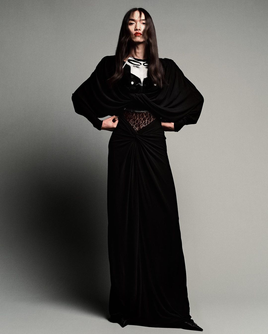 Full-length shot of an Asian fashion model in a black floor-length gown with an embellished top, striking a pose in a photo studio.