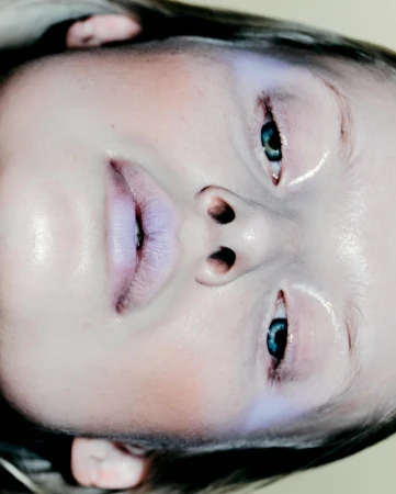 Close-up portrait of a model with glossy skin, pale lips, and dark eyes viewed from an upside-down perspective by Nick Yang.