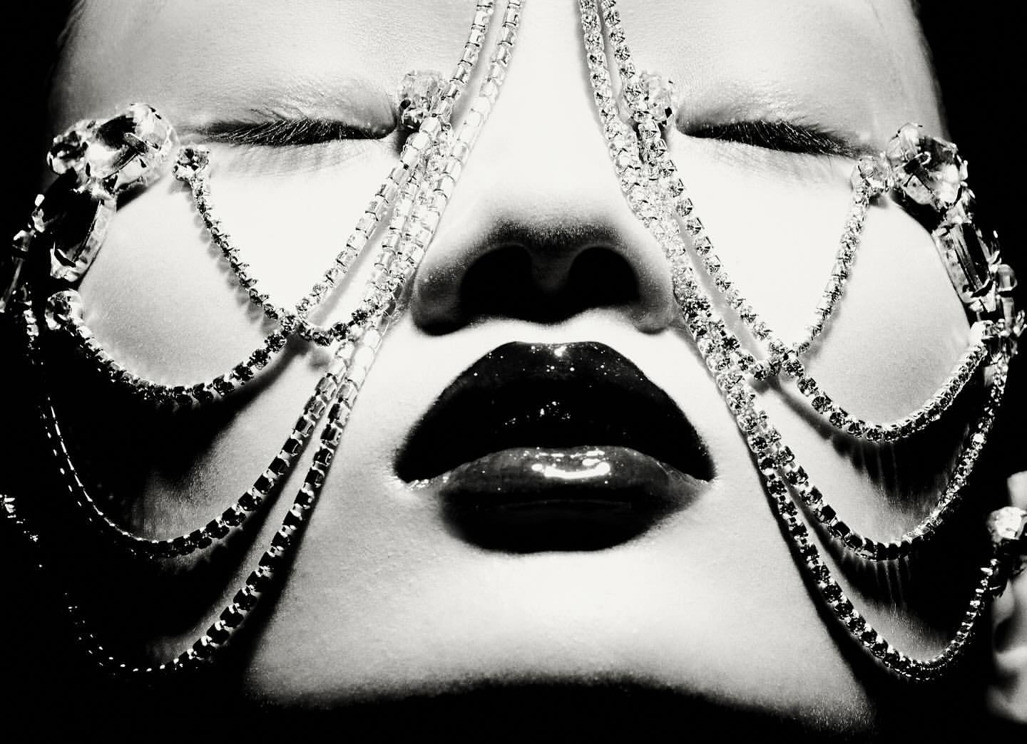 Close-up black and white portrait of a woman with closed eyes, glossy lips, and a jeweled headpiece.