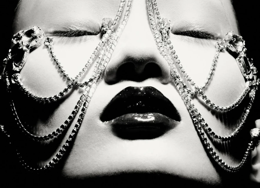 Close-up black and white portrait of a woman with closed eyes, glossy lips, and a jeweled headpiece.