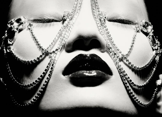 Close-up black and white portrait of a woman with closed eyes, glossy lips, and a jeweled headpiece.