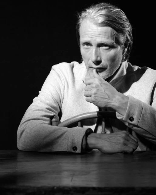 Black and white portrait of a light-skinned adult male with light hair wearing a light-colored collared shirt and wooden steering wheel.