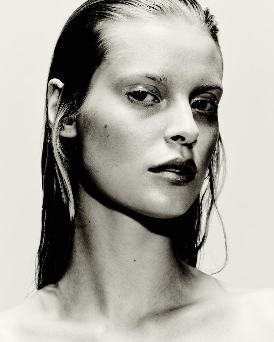 Close up portrait of a woman with wet hair and a serious expression against a plain white background
