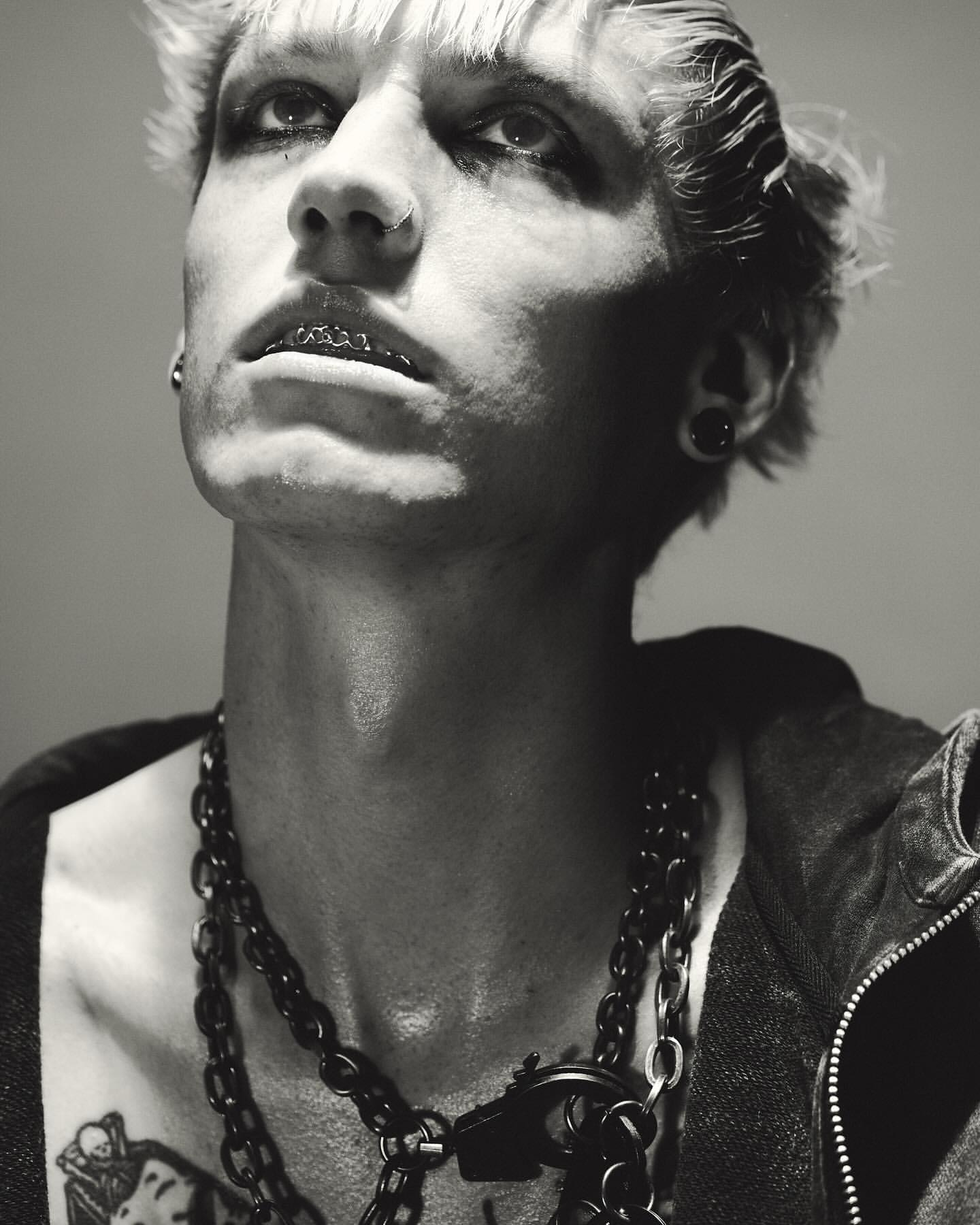 Portrait of a man with dyed blonde hair, dark eye makeup, nose ring, and layered chain necklaces captured by Nick Yang in Paris.