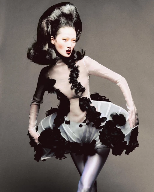 Avant-garde fashion portrait of an Asian woman with voluminous black hair, wearing a sheer white dress with black floral embellishments, studio shot.