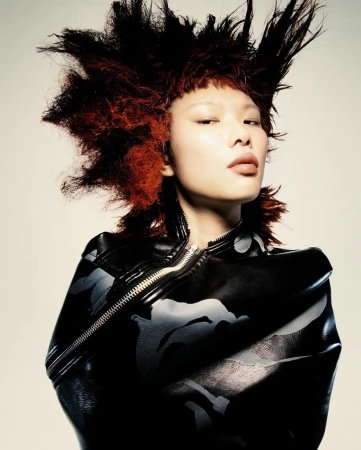 Portrait of a model with voluminous spiky red hair wearing a dark zip jacket against a plain light background by Nick Yang