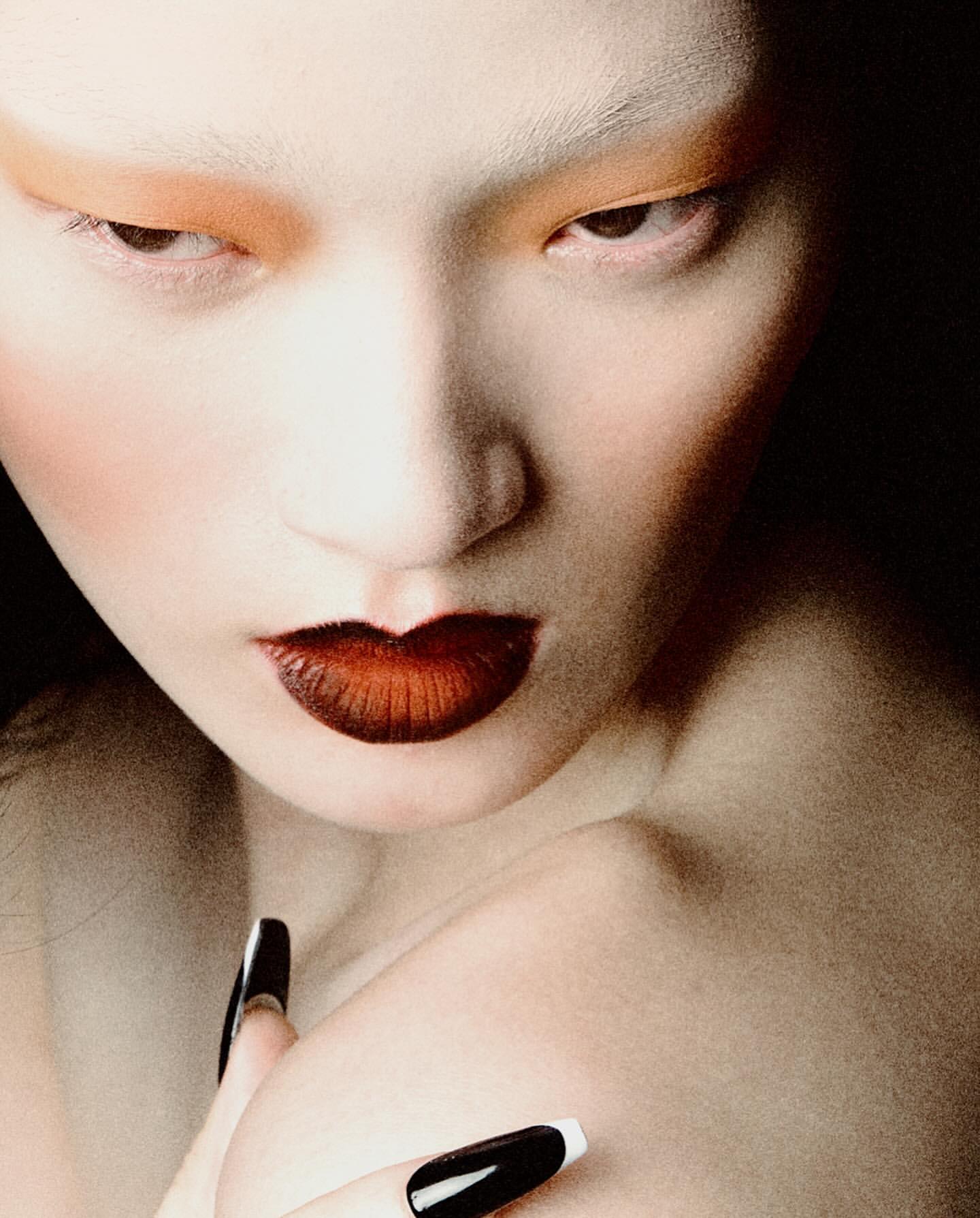 Striking beauty portrait with dramatic makeup, close-up on model's face, featuring bold lipstick, unique eye makeup, and stylized nail art.