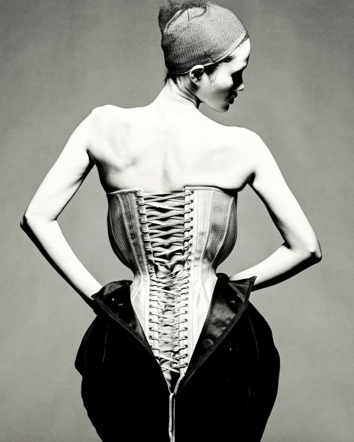 Monochrome back view of an adult female with a modern corset and visible lacing, accented by a partially unzipped dark coat.