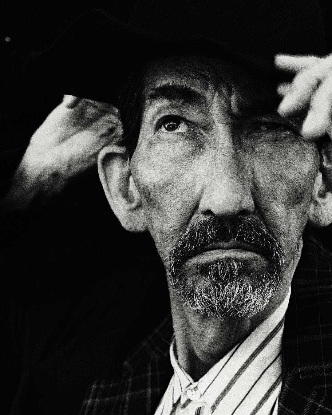 Monochrome portrait of an adult male with a mustache and goatee, wearing a patterned coat, and posing against a dark background.