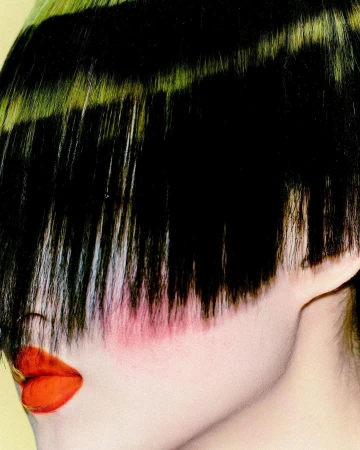 Close-up portrait of a model with blunt bangs covering eyes, bright orange lipstick, and pink blush by Nick Yang.