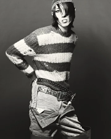 Striking black and white studio shot of androgynous person in distressed striped sweater and overalls, accessorized with studded belt and headpiece.