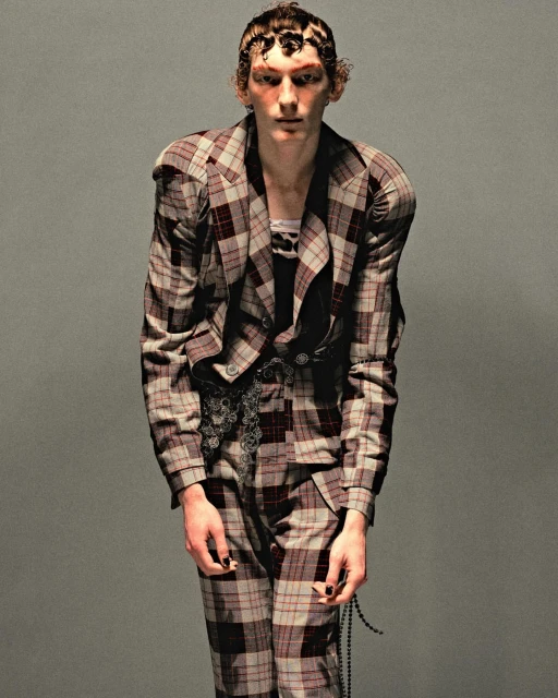 Fashion portrait of a model wearing a plaid suit. The background is grey. The subject is posed in a full-body shot indoors.