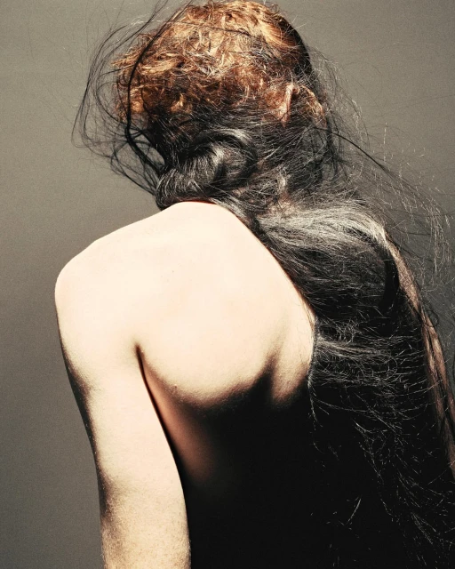 Back view of a person with long, dark hair and light skin against a dark gray background, showcasing textures and a natural, flowing hairstyle.