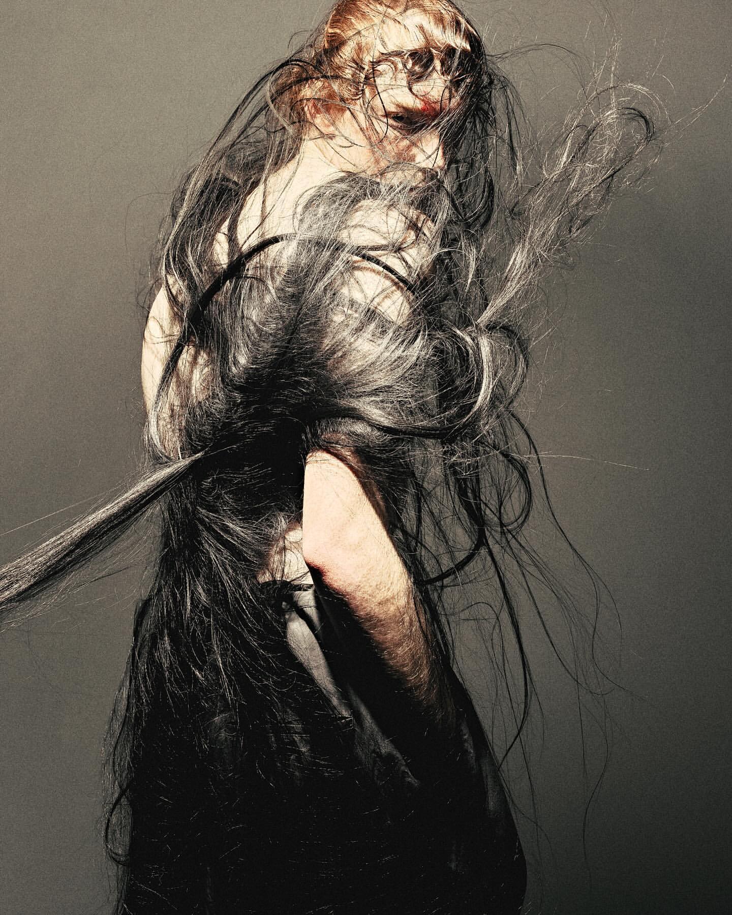 Model with long dark hair blowing across face in profile against a dark textured background