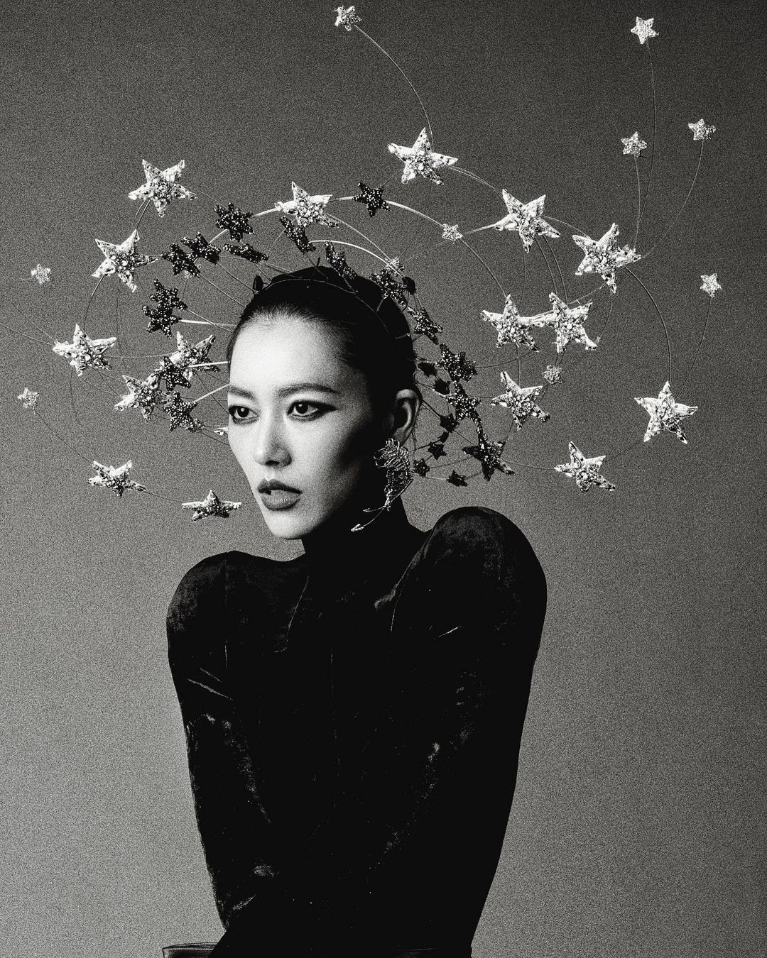 Asian woman in a black velvet dress and star headpiece posing in a studio. Fashion shot with glamourous and celestial vibes, black and white.