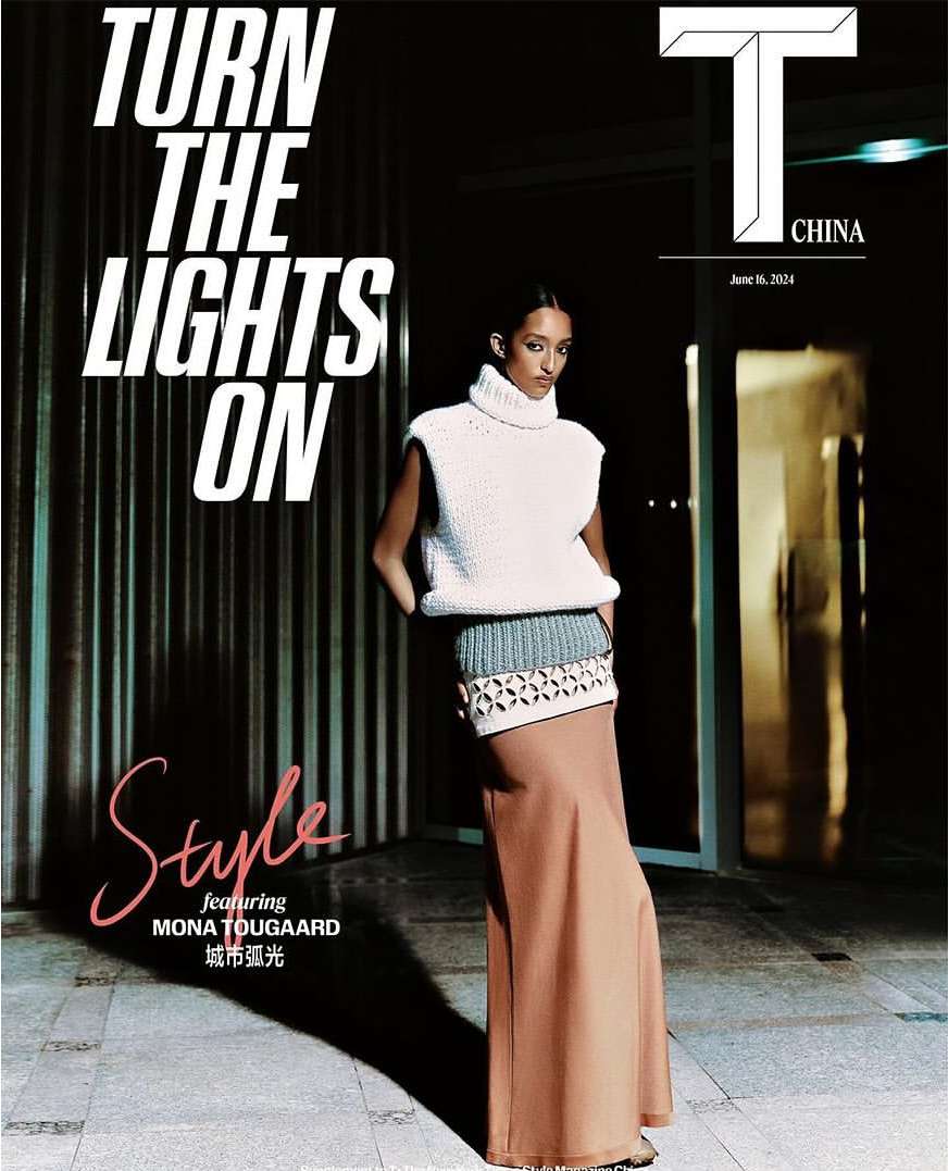 Fashion magazine cover featuring a model in a white turtleneck vest and long skirt standing on a concrete surface indoors with a door visible.