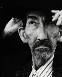 Close-up black and white portrait of a man wearing a hat and striped shirt by Nick Yang in Paris