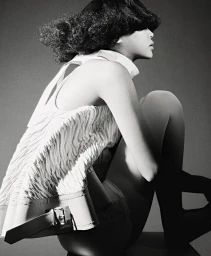 Monochrome studio portrait of a model with textured dark hair seated in profile wearing a textured white sleeveless top