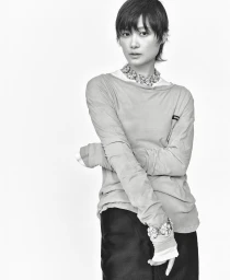 Monochrome portrait of a short-haired woman wearing a layered long-sleeve top and statement crystal necklace against a plain background