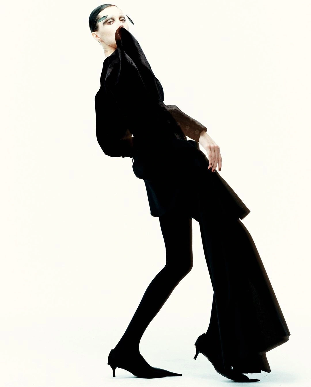 Model in black dress and tights posing dynamically against a bright white background in Paris by Nick Yang