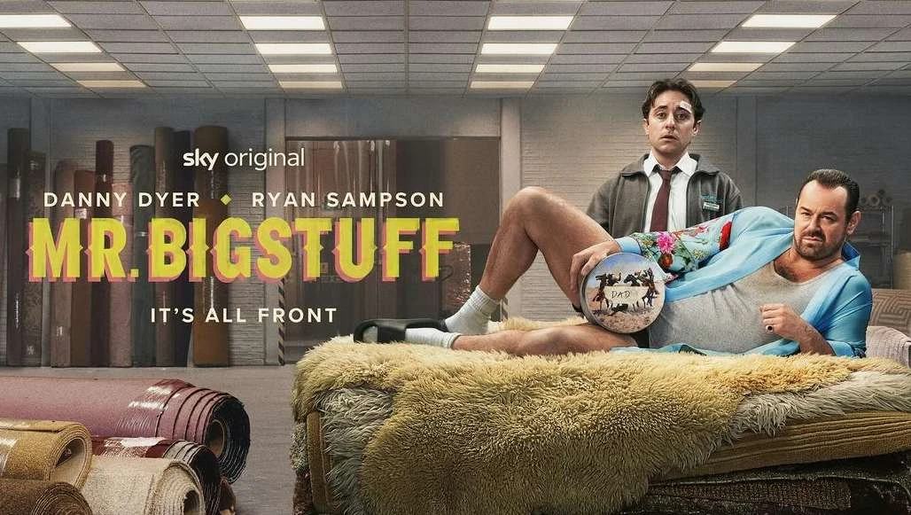 Promotional image for 'Mr. Bigstuff' features Danny Dyer reclining on a bed while Ryan Sampson stands behind in a carpet store setting.