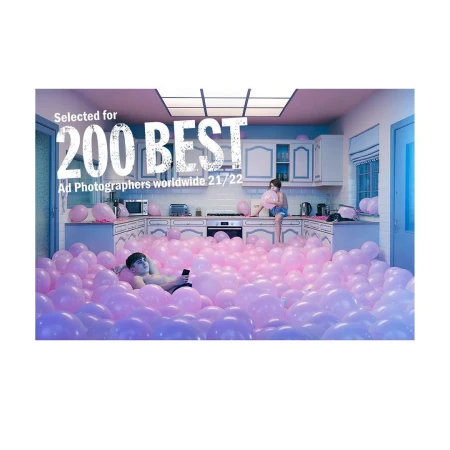 Man lounging in a kitchen filled with pink balloons and a child sitting on the counter holding a pink balloon