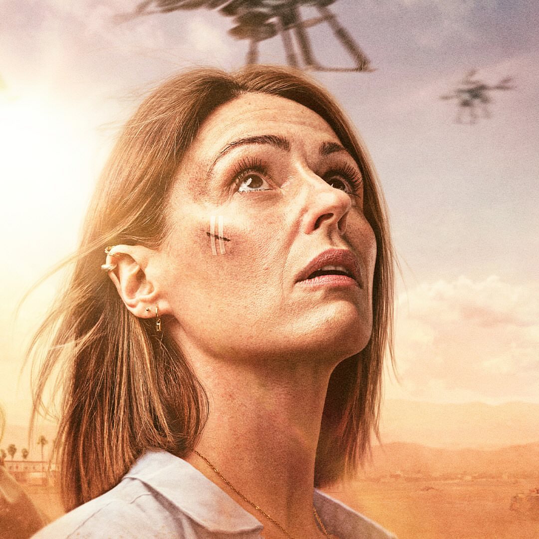 Close-up of a woman looking up at drones in the sky, with scratches on her face, against a landscape backdrop under a light sky.