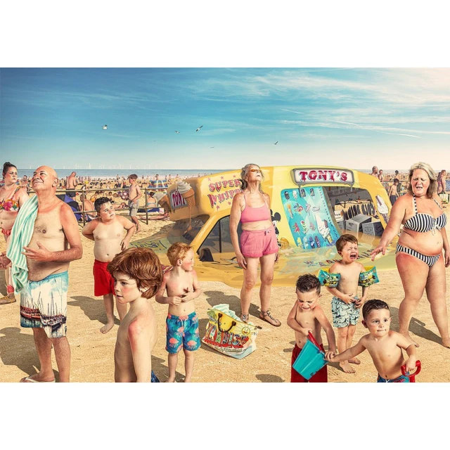 A group of people are gathered around a yellow ice cream van on a sandy beach under a bright blue sky dotted with a few birds.