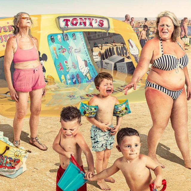 Family gathers on sandy beach near a vintage ice cream truck on a sunny day; boys with arm floaties and swimwear. A woman stands watching.