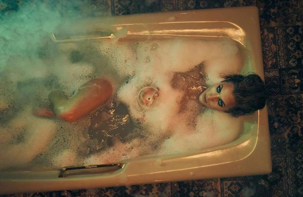 Woman relaxes in a bubble bath, gazing upward with dramatic lighting and tiled surroundings, creating a surreal, moody atmosphere.