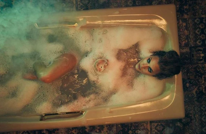 Woman relaxes in a bubble bath, gazing upward with dramatic lighting and tiled surroundings, creating a surreal, moody atmosphere.