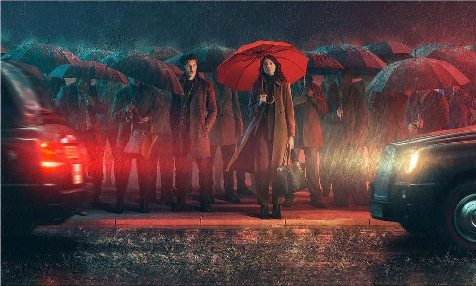 Two people stand amidst a crowd under umbrellas on a rainy street, with cars and city lights adding depth to the scene.