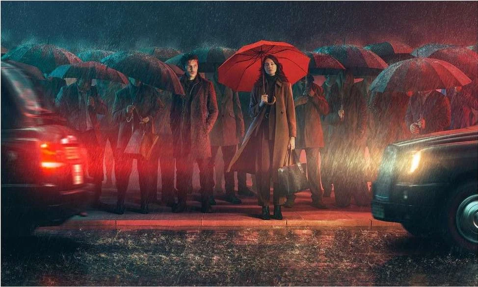 Two people stand amidst a crowd under umbrellas on a rainy street, with cars and city lights adding depth to the scene.
