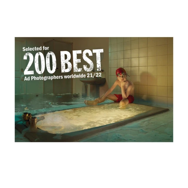Young boy in a red swim cap and shorts sits on the edge of a tiled tub in a vintage bathroom.  Award text overlay in the top left corner.