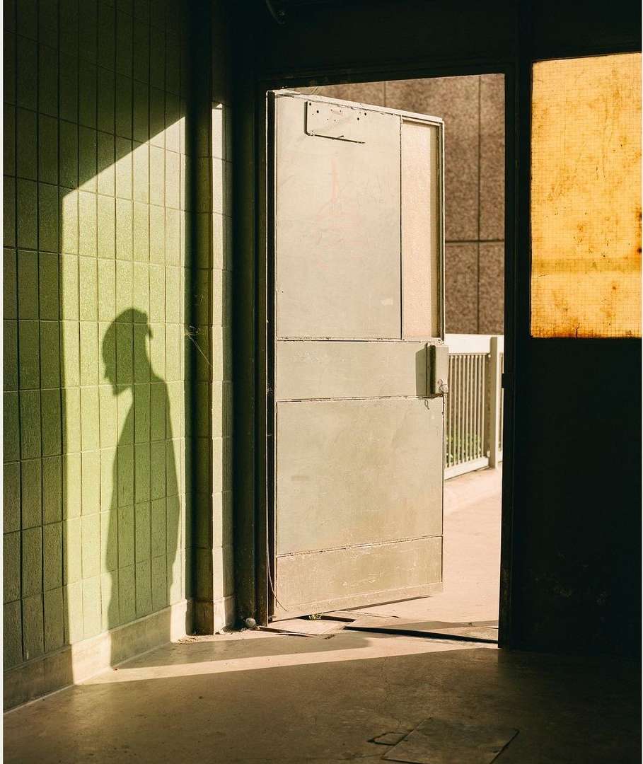 Indoor view of light illuminating tiled wall, with silhouette of a person and partially open metal door. Architectural photo.