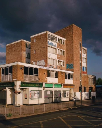 Exterior view of a multi-story brick building with a row of shops below, under a cloudy sky, in a city setting with street.