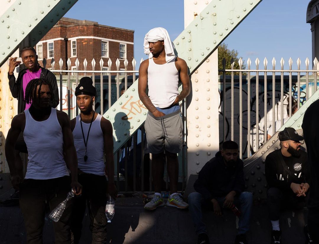 Outdoor portrait of seven young adult men on a bridge, dressed in casual attire, captured in natural light with an urban backdrop.