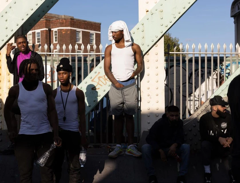 Outdoor portrait of seven young adult men on a bridge, dressed in casual attire, captured in natural light with an urban backdrop.