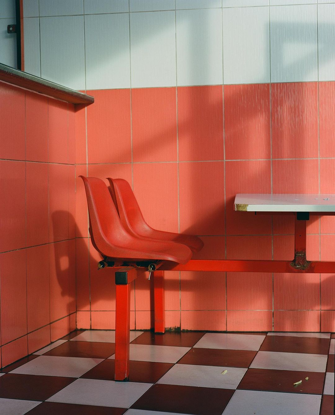 A photograph shows a red diner-style table and attached chairs in a tiled room with a checkered floor and cool, even lighting.