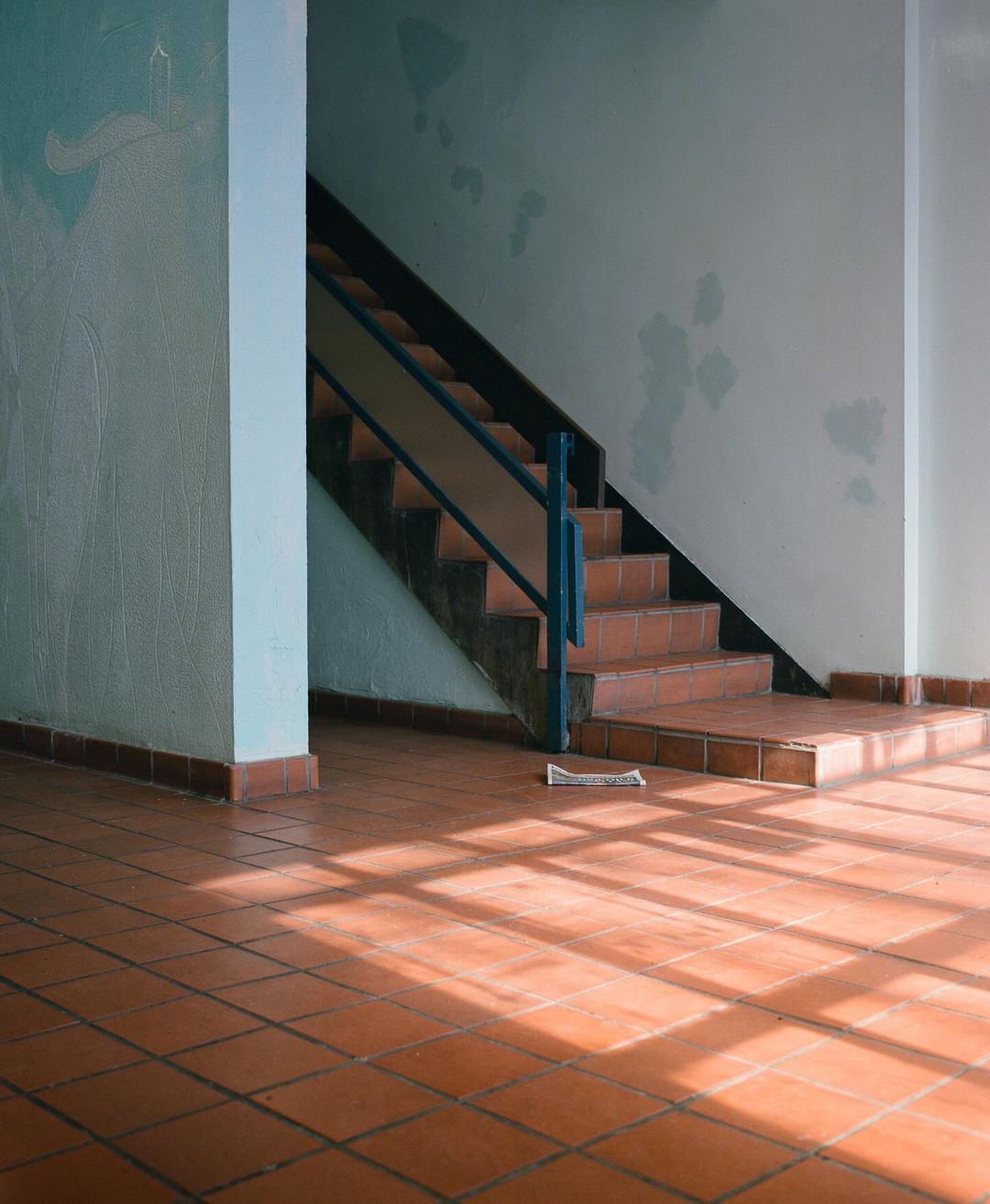 Indoor stairway with red brick steps and landing, blue metal railing, and natural lighting in a minimalist interior space.