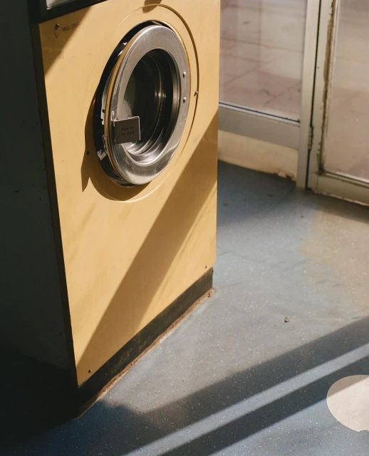 Commercial laundry machine in a laundromat bathed in natural light and shadow creating geometric patterns on the floor.