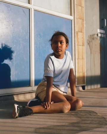 Young child seated on concrete outdoors wearing light blue t-shirt and shorts, photographed by Nico Froehlich.