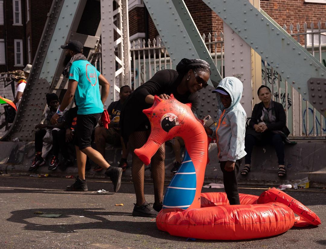 Adult and child on city street with inflatable sea dragon, buildings and bridge visible in the background on a sunny day.