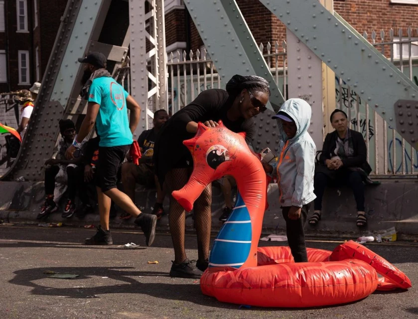 Adult and child on city street with inflatable sea dragon, buildings and bridge visible in the background on a sunny day.