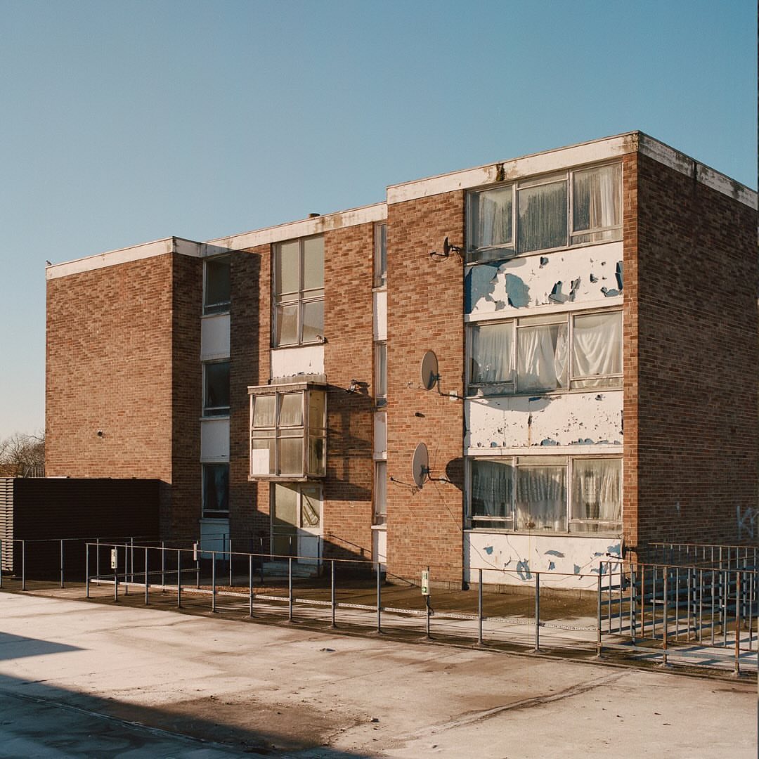 Exterior of a three-story brick apartment building under a clear blue sky, featuring white window frames and symmetrical satellite dishes.