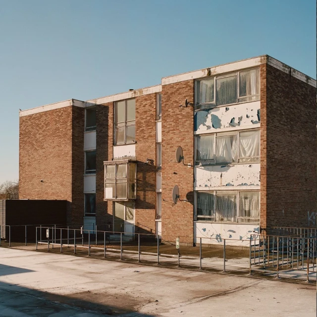 Exterior of a three-story brick apartment building under a clear blue sky, featuring white window frames and symmetrical satellite dishes.