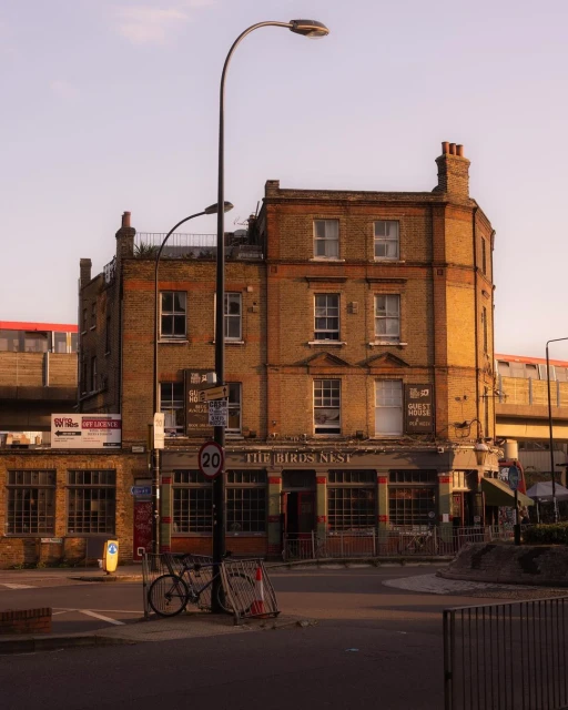 Exterior view of The Birds Nest pub in London, England, featuring its brick facade, street lamp, and bicycle parked nearby on a sunny day.